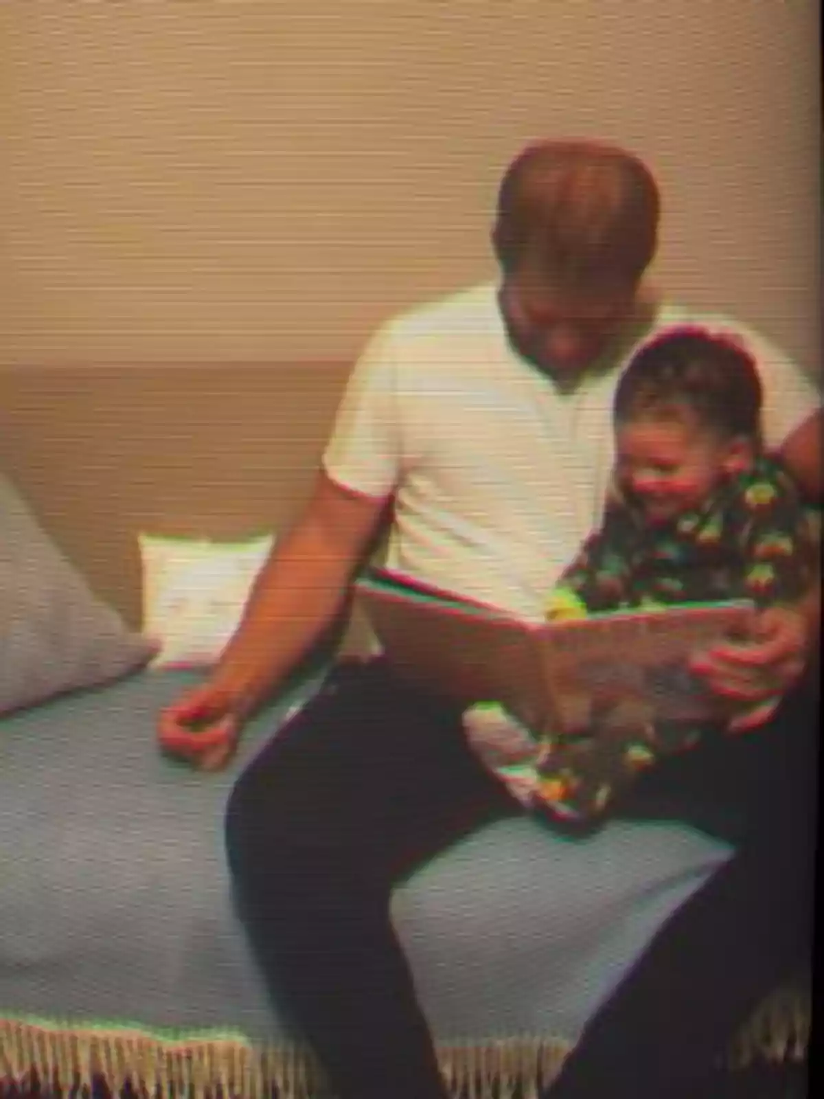 Prince Harry and Archie sitting on a couch reading a book together and smiling Prince Harry and Archie sitting on a couch reading a book together and smiling