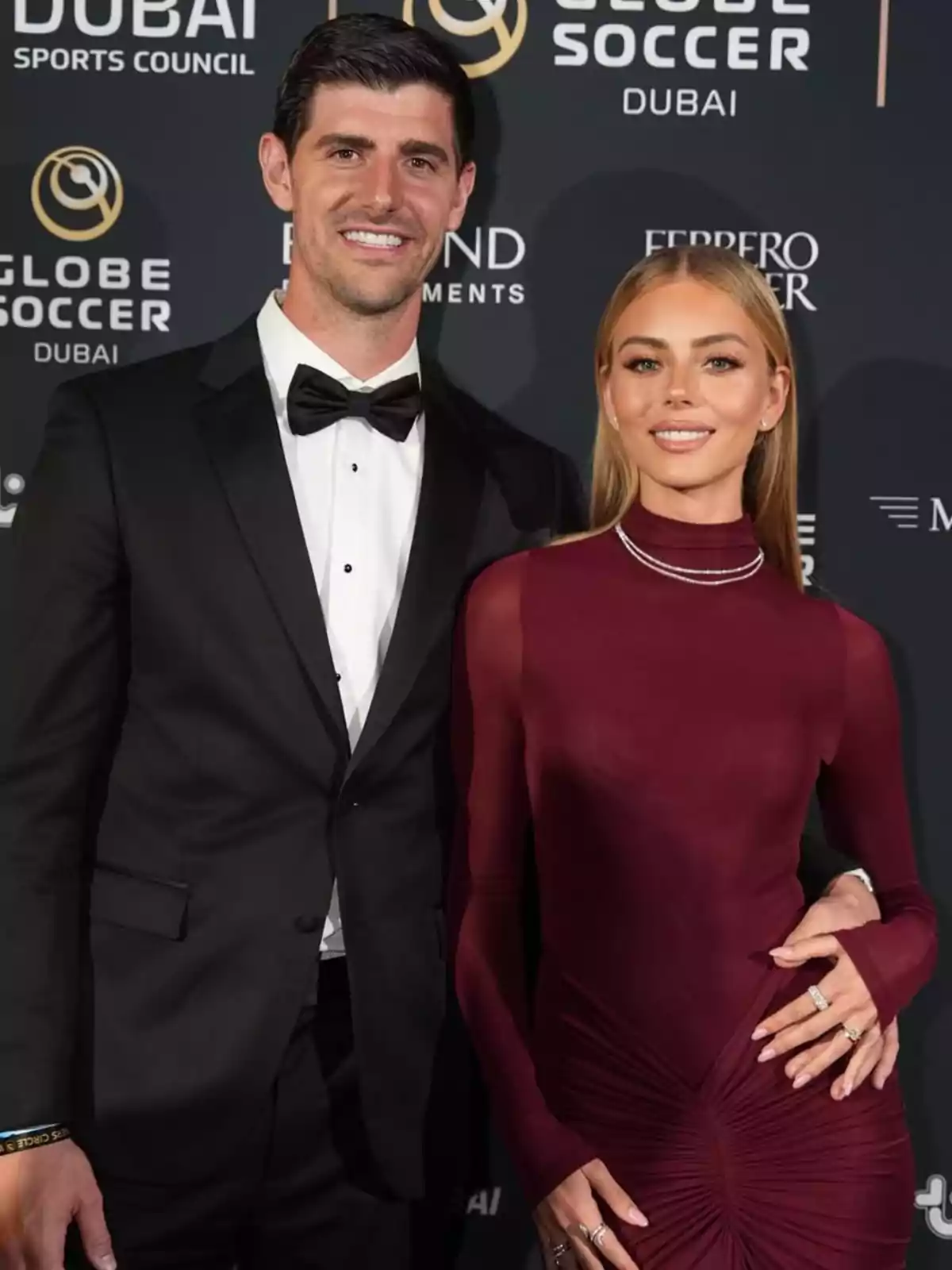 Thibaut Courtois i Mishel Gerzig elegantment vestida posen en un esdeveniment de gala amb un fons de logotips de Globe Soccer a Dubai. Thibaut Courtois i Mishel Gerzig elegantment vestida posen en un esdeveniment de gala amb un fons de logotips de Globe Soccer a Dubai.