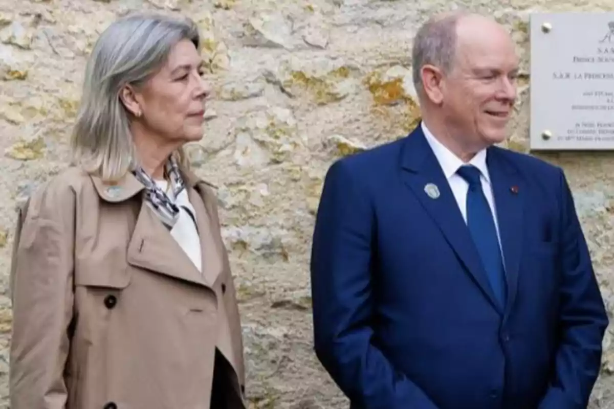Carolina y Alberto de Mónaco de pie frente a una pared de piedra una mujer con abrigo beige y un hombre con traje azul sonriente Carolina y Alberto de Mónaco de pie frente a una pared de piedra una mujer con abrigo beige y un hombre con traje azul sonriente