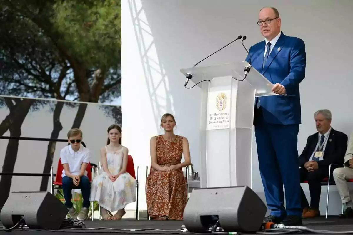 Albert de Mònaco amb vestit blau parla en un faristol durant un esdeveniment a l’aire lliure mentre diverses persones, incloent-hi dos nens i una dona, estan assegudes darrere seu. Albert de Mònaco amb vestit blau parla en un faristol durant un esdeveniment a l’aire lliure mentre diverses persones, incloent-hi dos nens i una dona, estan assegudes darrere seu.
