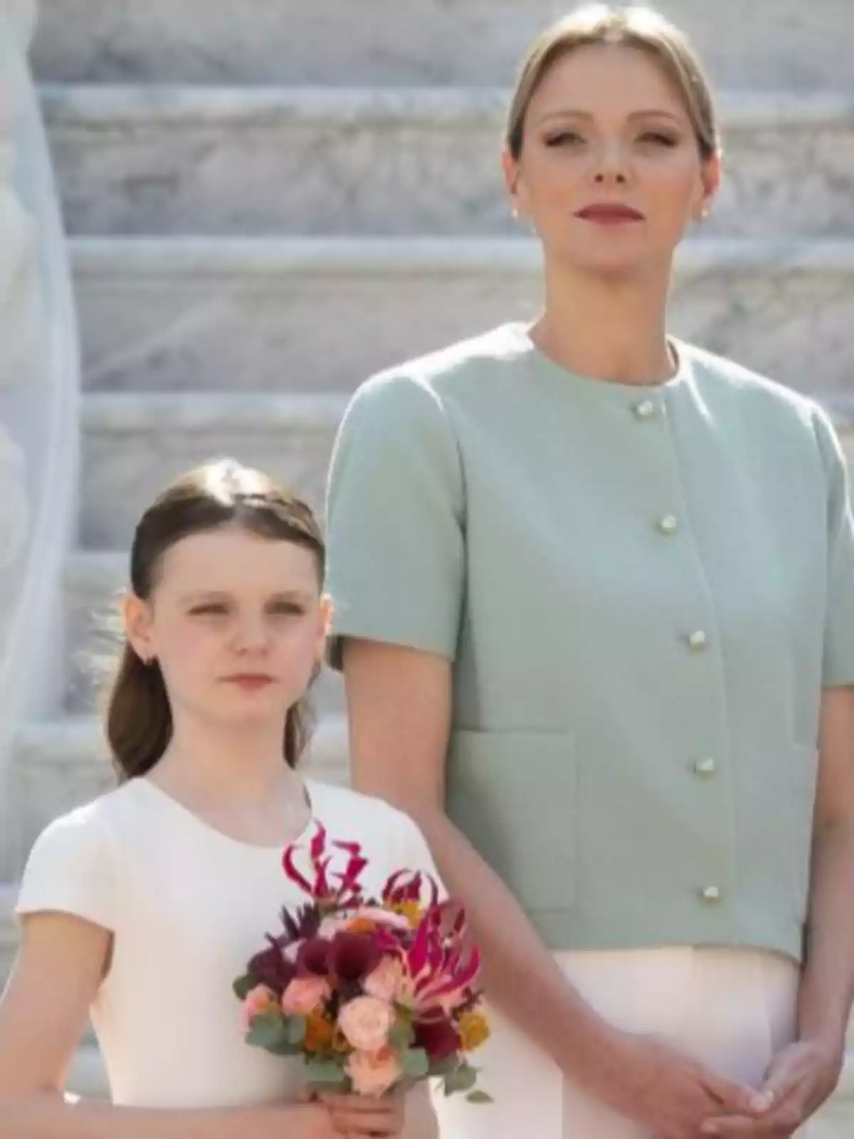 Charlene i Gabriella de Mònaco posen juntes en una escala de marbre, la nena sosté un ram de flors i ambdues miren al davant amb expressió seriosa. Charlene i Gabriella de Mònaco posen juntes en una escala de marbre, la nena sosté un ram de flors i ambdues miren al davant amb expressió seriosa.