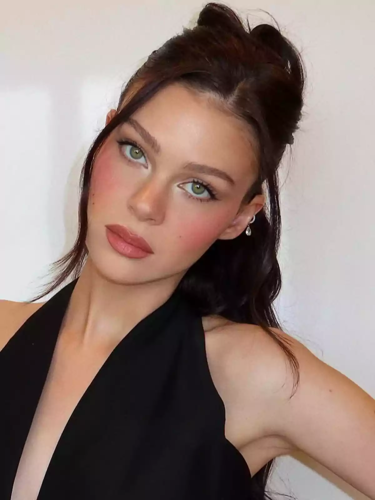 Nicola Peltz, wearing a sleeveless black dress, poses in front of a white background. Nicola Peltz, wearing a sleeveless black dress, poses in front of a white background.