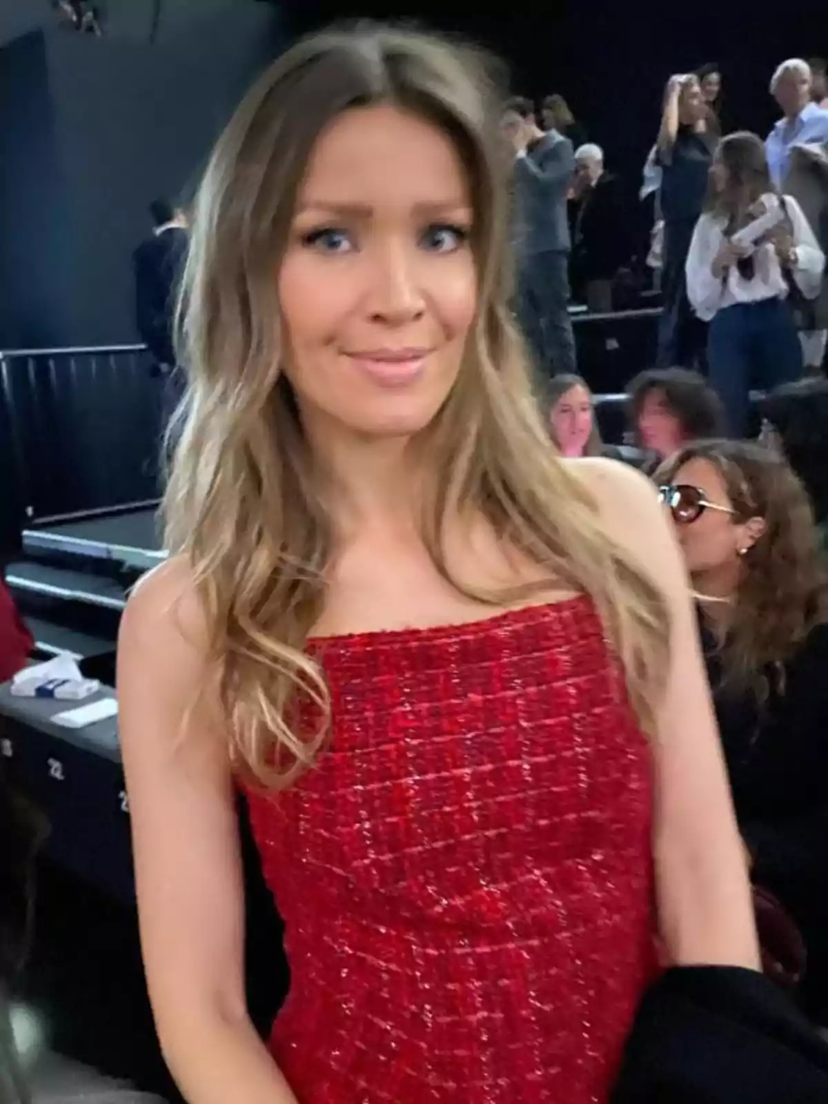 Nicole Kimpel con un vestido rojo posando en un evento con varias personas al fondo.