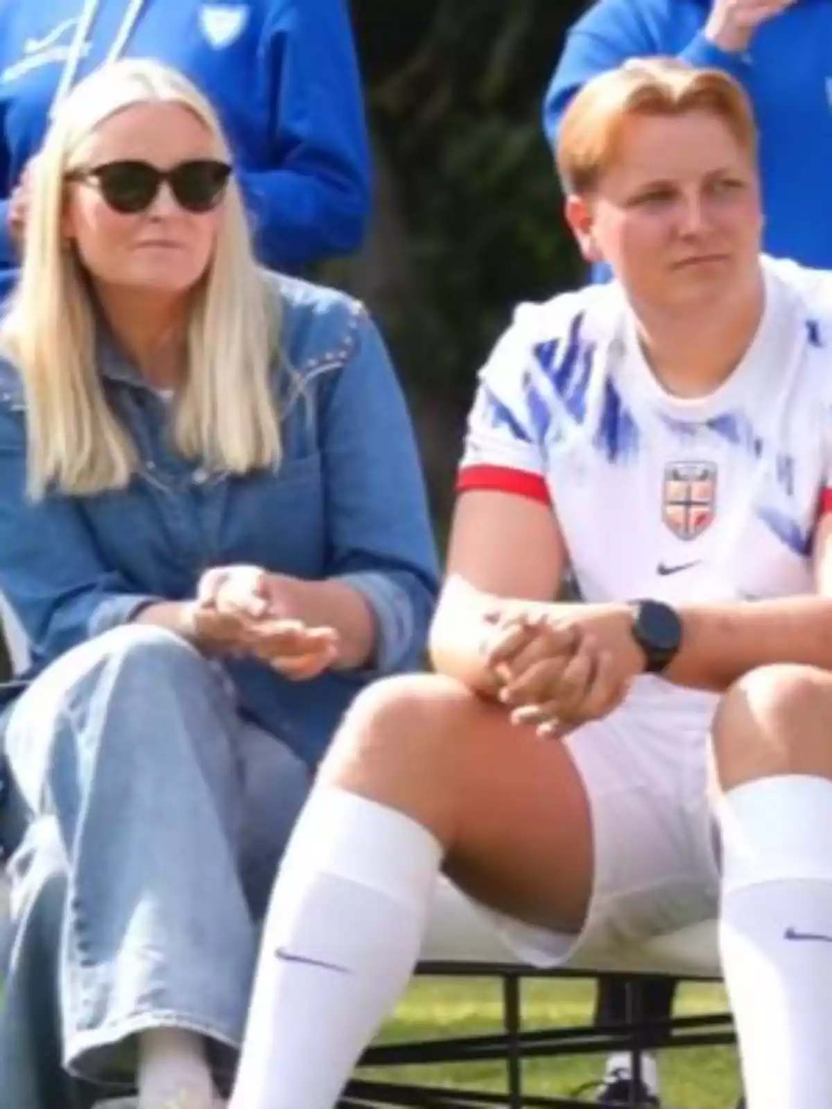 Mette-Marit and Sverre of Norway sitting outdoors, one wearing sunglasses and denim clothing and the other in a white sports uniform. Mette-Marit and Sverre of Norway sitting outdoors, one wearing sunglasses and denim clothing and the other in a white sports uniform.