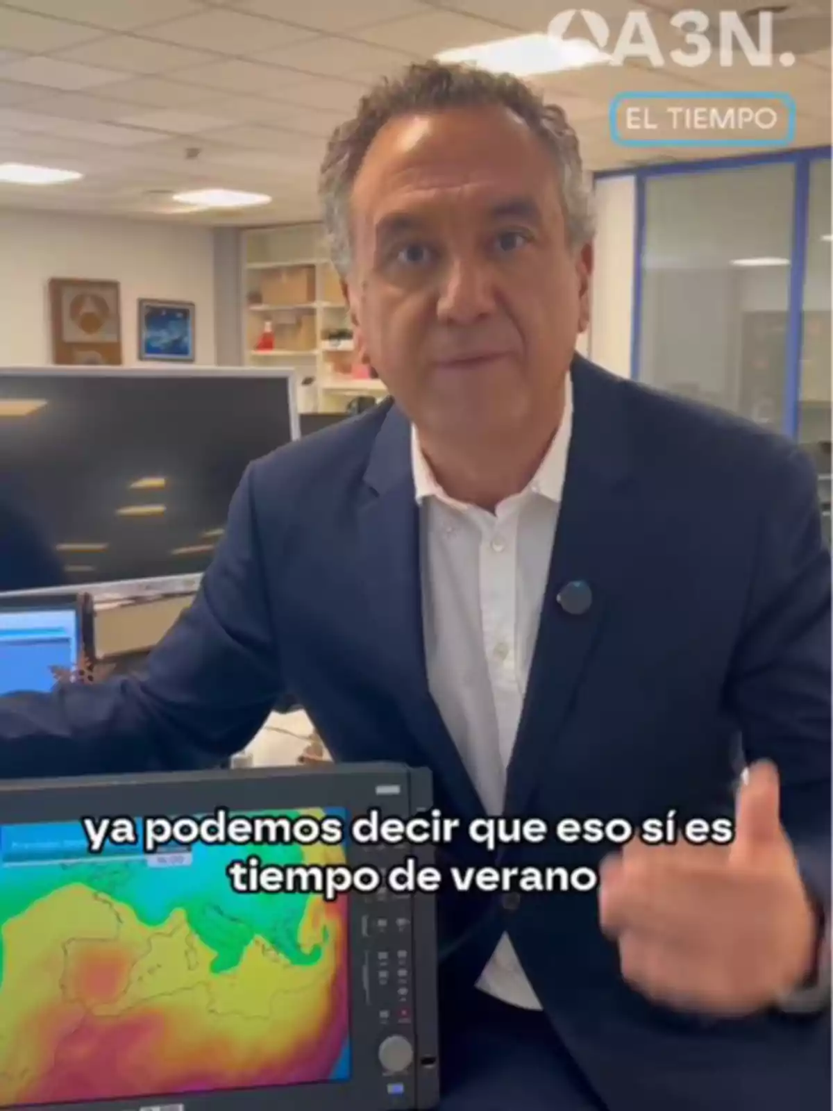 Un home en una oficina assenyala una pantalla que mostra un mapa meteorològic amb colors càlids i el text Un home en una oficina assenyala una pantalla que mostra un mapa meteorològic amb colors càlids i el text