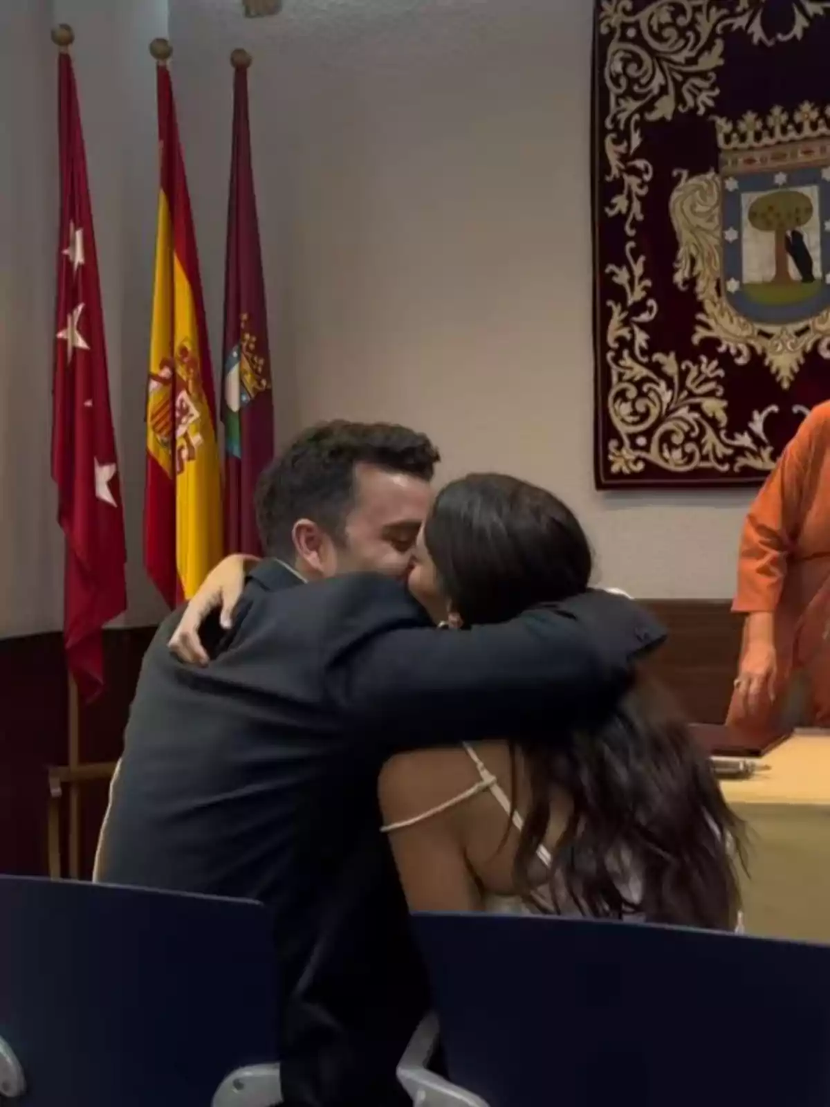 Guille Valle i Susana Molina s’abracen i es fan un petó asseguts en una sala amb banderes i un tapís decoratiu al fons. Guille Valle i Susana Molina s’abracen i es fan un petó asseguts en una sala amb banderes i un tapís decoratiu al fons.