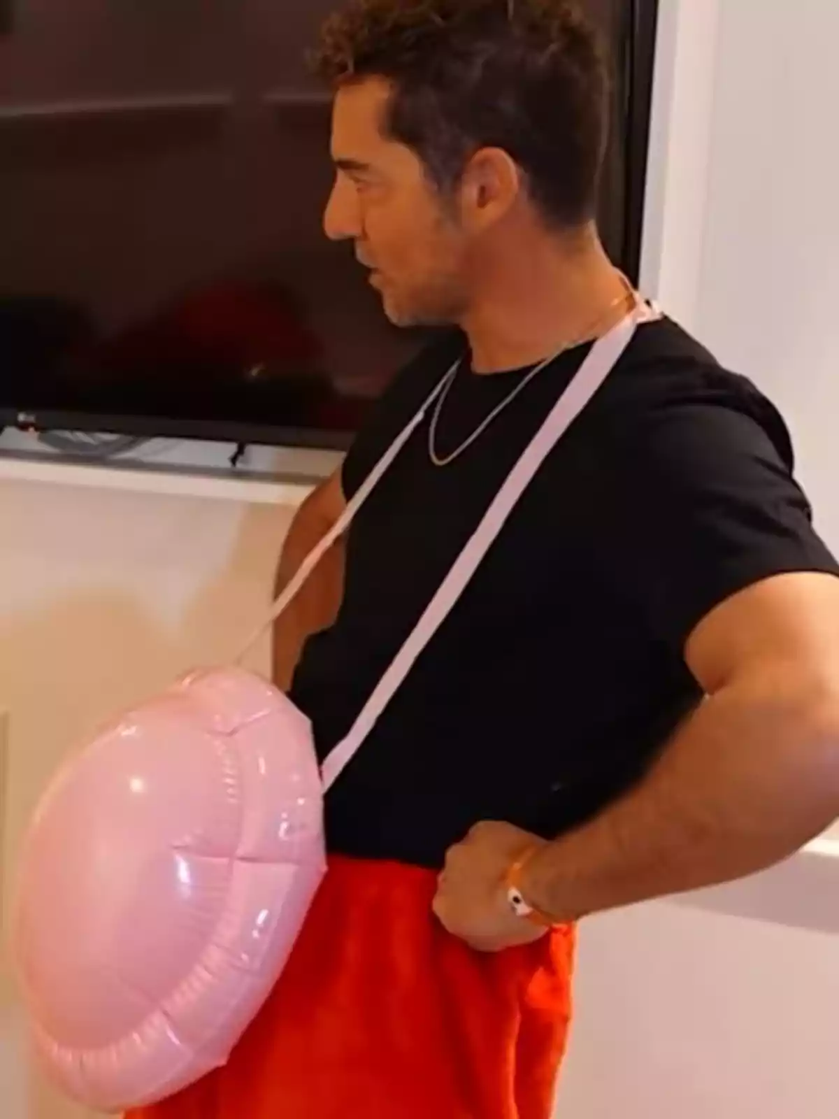 David Bisbal amb una samarreta negra i pantalons vermells porta un objecte inflable rosa penjat al coll. David Bisbal amb una samarreta negra i pantalons vermells porta un objecte inflable rosa penjat al coll.