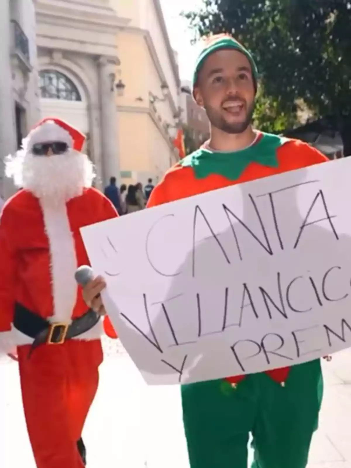 David Bisbal i The Grefg disfressades de Santa Claus i elf sostenen un cartell que convida a cantar nadales en un carrer. David Bisbal i The Grefg disfressades de Santa Claus i elf sostenen un cartell que convida a cantar nadales en un carrer.