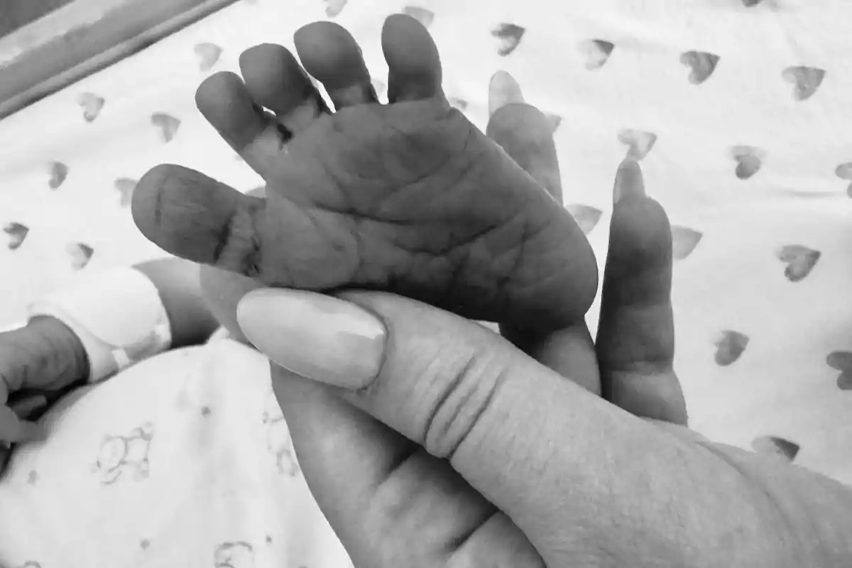Una mà adulta sosté el peu d'un nadó sobre una manta amb estampat de cors. Una mà adulta sosté el peu d'un nadó sobre una manta amb estampat de cors.
