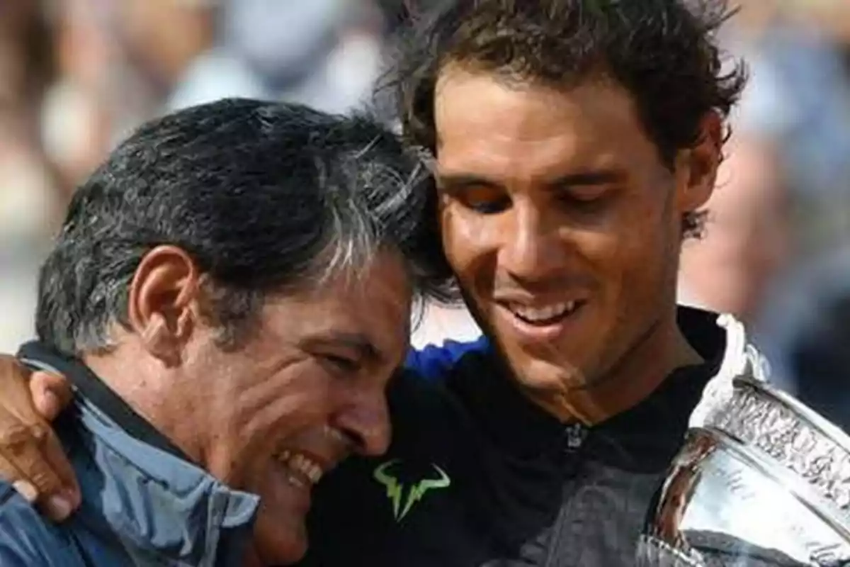 Toni y Rafa Nadal sonríen y se abrazan mientras una de ellas sostiene un trofeo plateado.