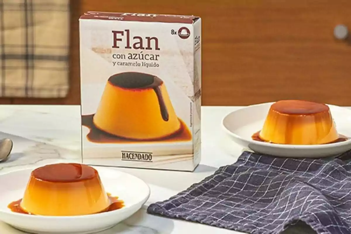 Caixa de flam amb sucre i caramel líquid de la marca Hacendado al costat de dues porcions de flam servides en plats blancs sobre una taula amb un drap blau. Caixa de flam amb sucre i caramel líquid de la marca Hacendado al costat de dues porcions de flam servides en plats blancs sobre una taula amb un drap blau.