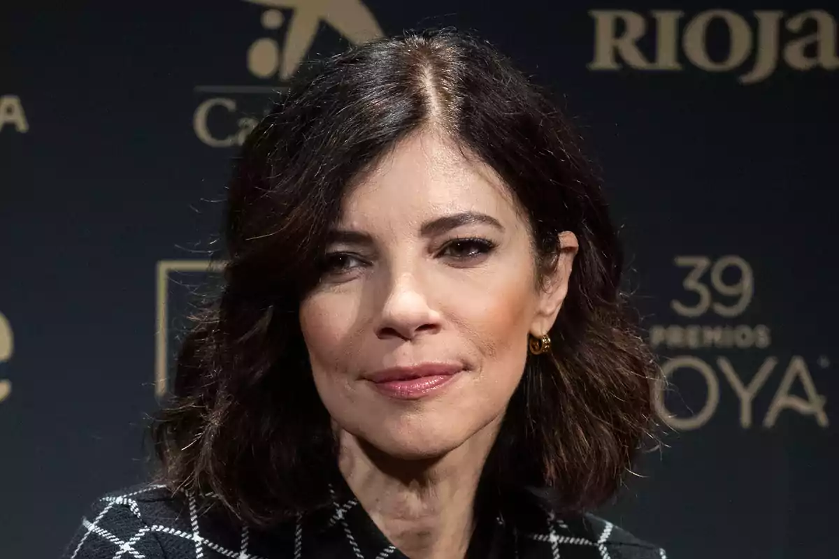 Maribel Verdú con cabello oscuro y corto, usando aretes dorados, en un evento con fondo oscuro y logotipos. Maribel Verdú con cabello oscuro y corto, usando aretes dorados, en un evento con fondo oscuro y logotipos.