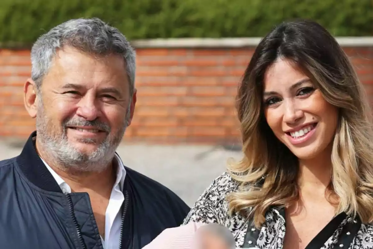 Miki Nadal i Helena Aldea somriuen a la cambra mentre sostenen un nadó, amb un fons de maons i vegetació.