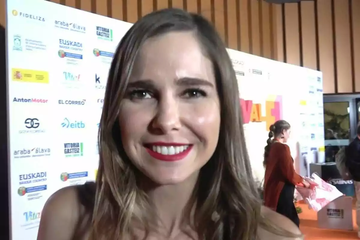Natalia Sánchez somrient en un esdeveniment amb un fons de logotips i una persona en segon pla. Natalia Sánchez somrient en un esdeveniment amb un fons de logotips i una persona en segon pla.