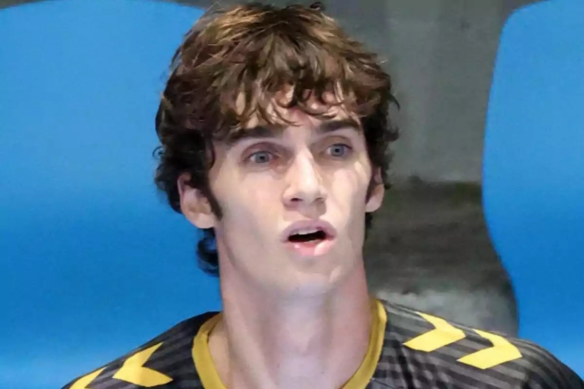 Pablo Urdangarin amb expressió de sorpresa i cabell arrissat, vestint una samarreta esportiva negra amb detalls grocs, assegut davant d'un fons blau. Pablo Urdangarin amb expressió de sorpresa i cabell arrissat, vestint una samarreta esportiva negra amb detalls grocs, assegut davant d'un fons blau.