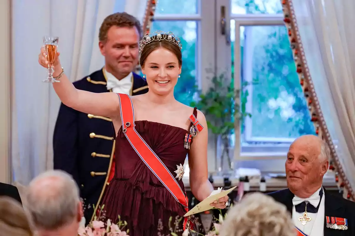 La princesa Ingrid Alexandra de Noruega amb vestit elegant i diadema aixeca una copa en un brindis mentre somriu, envoltada de persones en un esdeveniment formal. La princesa Ingrid Alexandra de Noruega amb vestit elegant i diadema aixeca una copa en un brindis mentre somriu, envoltada de persones en un esdeveniment formal.