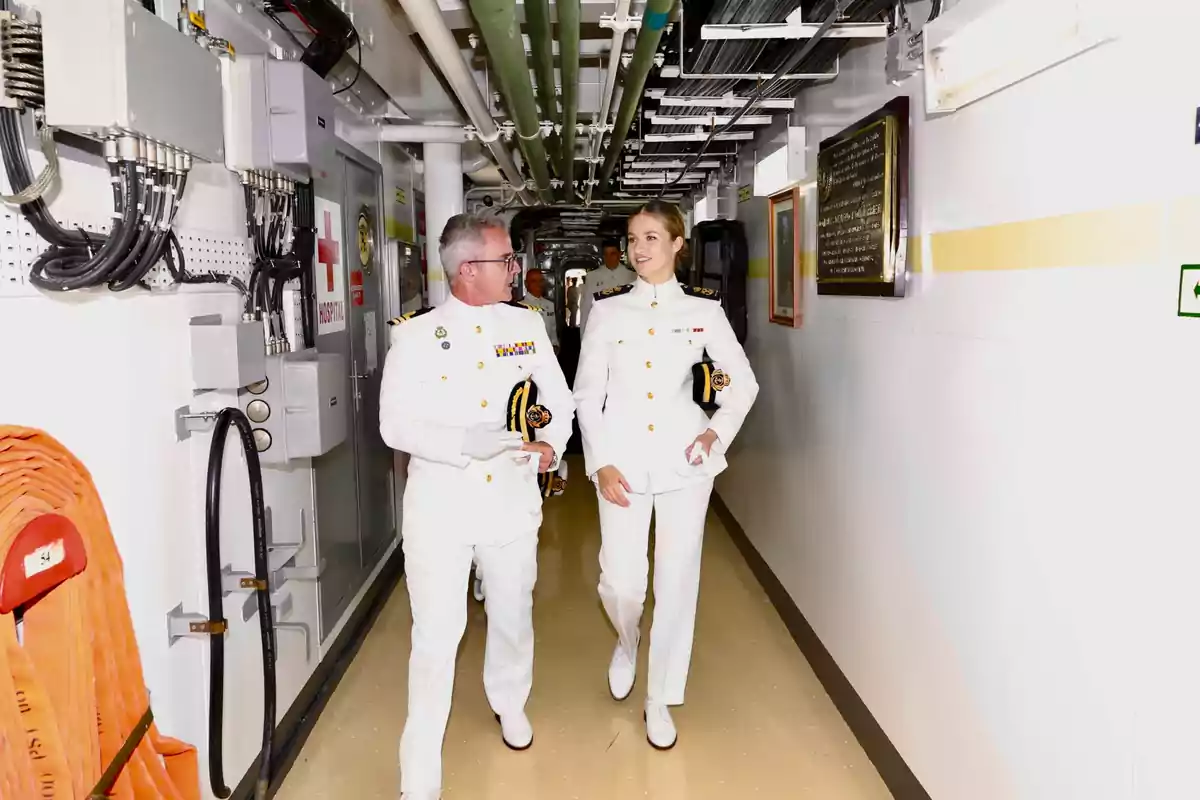 Elionor amb uniforme blanc de gala de la marina camina per un passadís d'un vaixell mentre conversa i somriu Elionor amb uniforme blanc de gala de la marina camina per un passadís d'un vaixell mentre conversa i somriu