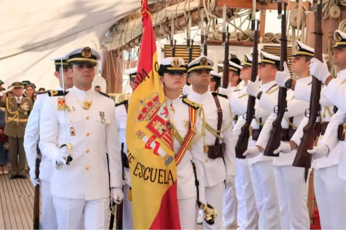 Grup d'oficials navals en uniforme blanc sostenint una bandera i fusells durant una cerimònia en un vaixell. Grup d'oficials navals en uniforme blanc sostenint una bandera i fusells durant una cerimònia en un vaixell.
