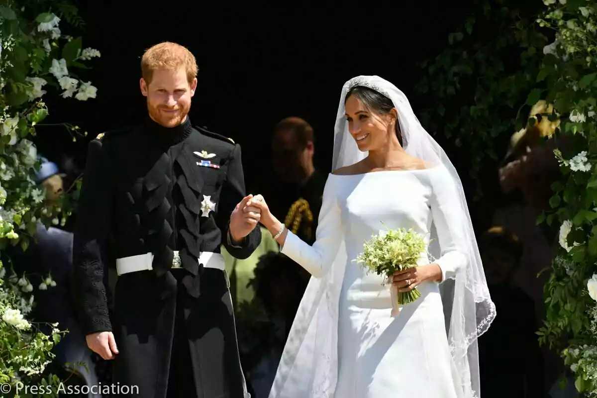 El príncep Harry i Meghan Markle somrient vestida de nuvis surt d'un edifici decorat amb flors. El príncep Harry i Meghan Markle somrient vestida de nuvis surt d'un edifici decorat amb flors.