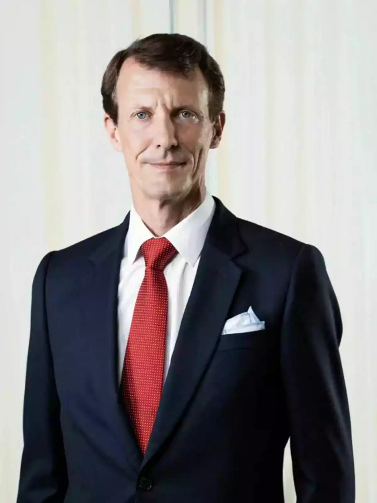 Prince Joachim of Denmark wearing a navy blue suit with a red tie and a white jersey posing in front of a light background Prince Joachim of Denmark wearing a navy blue suit with a red tie and a white jersey posing in front of a light background