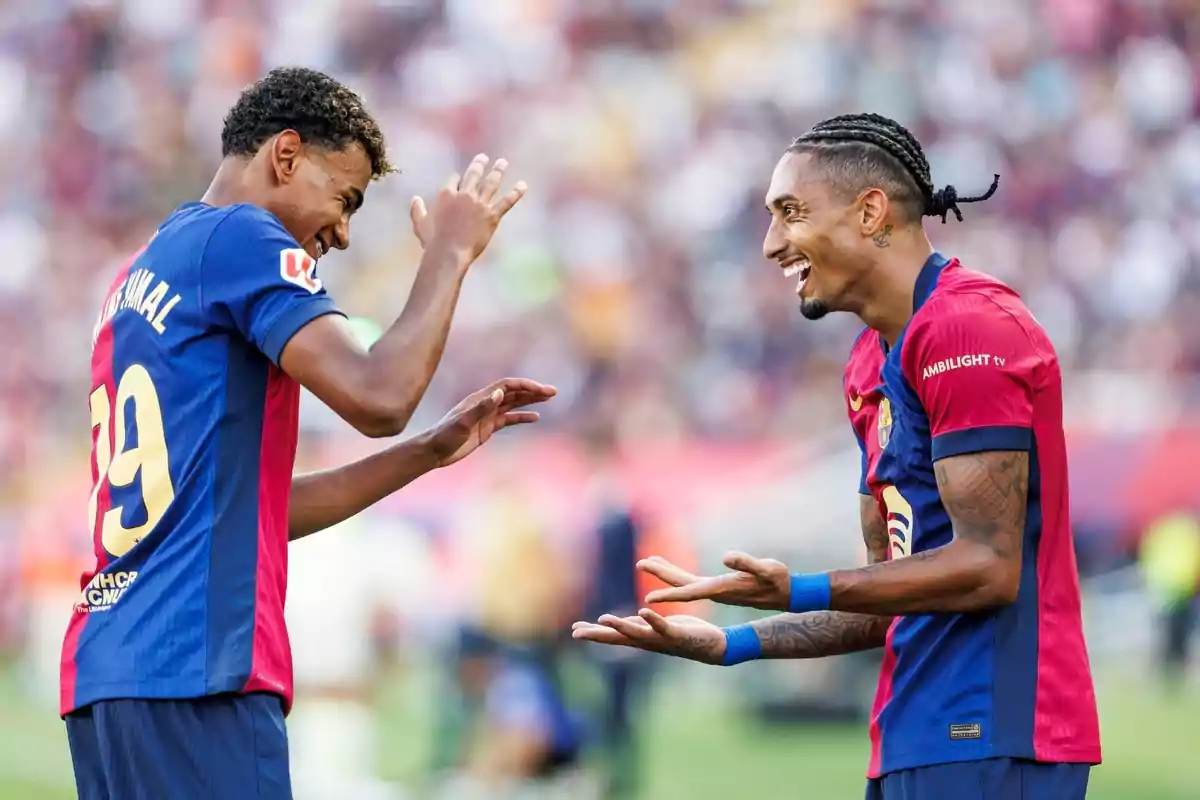 Dos jugadors de futbol amb uniformes blau i vermell somriuen i gesticulen al camp. Dos jugadors de futbol amb uniformes blau i vermell somriuen i gesticulen al camp.
