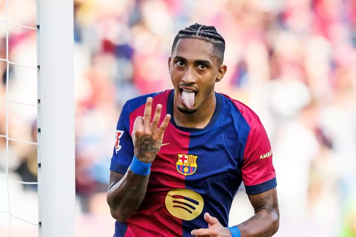 Jugador de fútbol con la camiseta del FC Barcelona celebrando un gol con la lengua afuera y mostrando tres dedos.