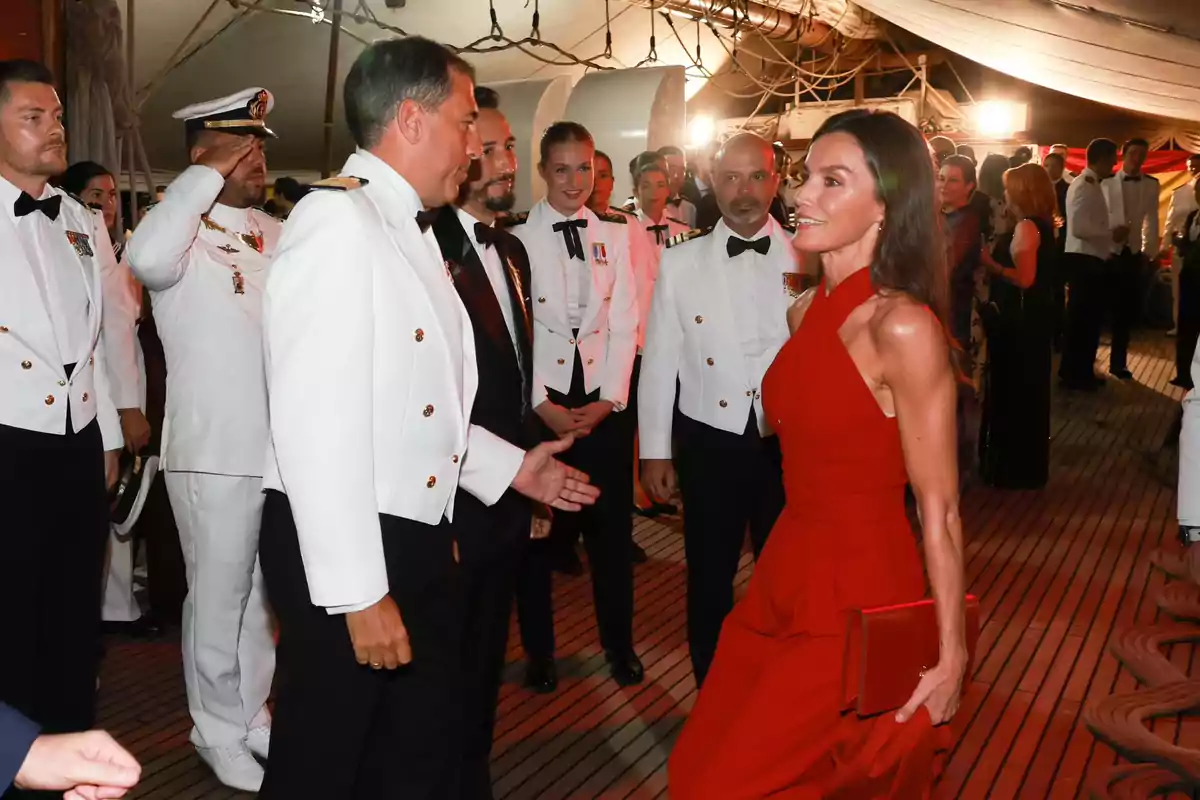 La reina Letizia, juntament amb un grup de persones vestides de gala, interactua en un esdeveniment formal a bord d'un vaixell. La reina Letizia, juntament amb un grup de persones vestides de gala, interactua en un esdeveniment formal a bord d'un vaixell.