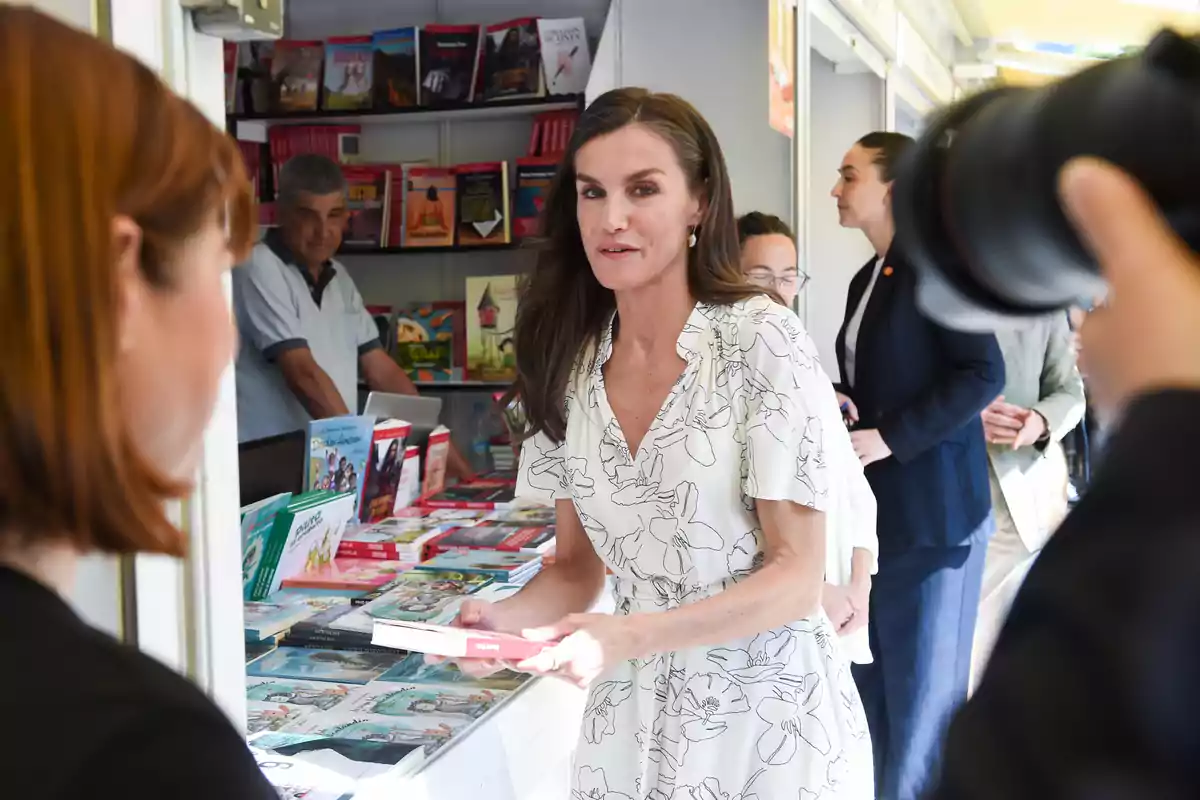 Queen Letizia in a white dress with black stripes holding a book at a fair Queen Letizia in a white dress with black stripes holding a book at a fair