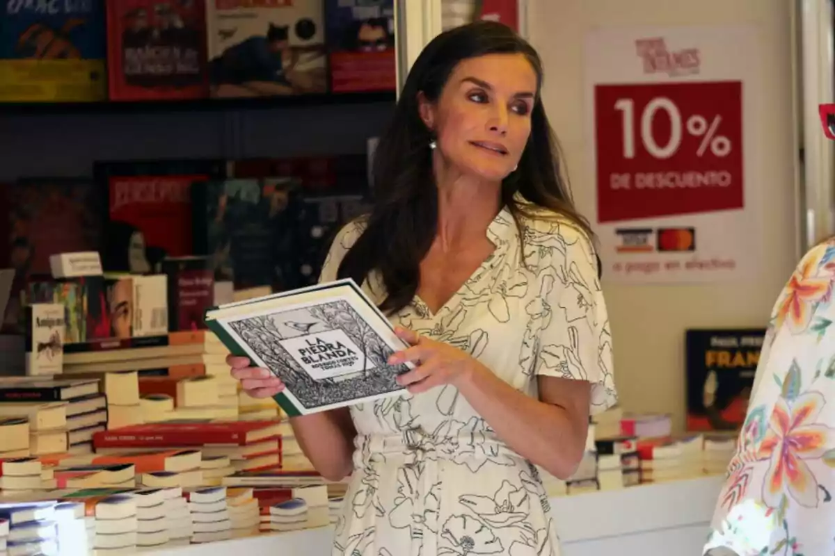 Queen Letizia, wearing a light-colored dress, holds a book titled Queen Letizia, wearing a light-colored dress, holds a book titled