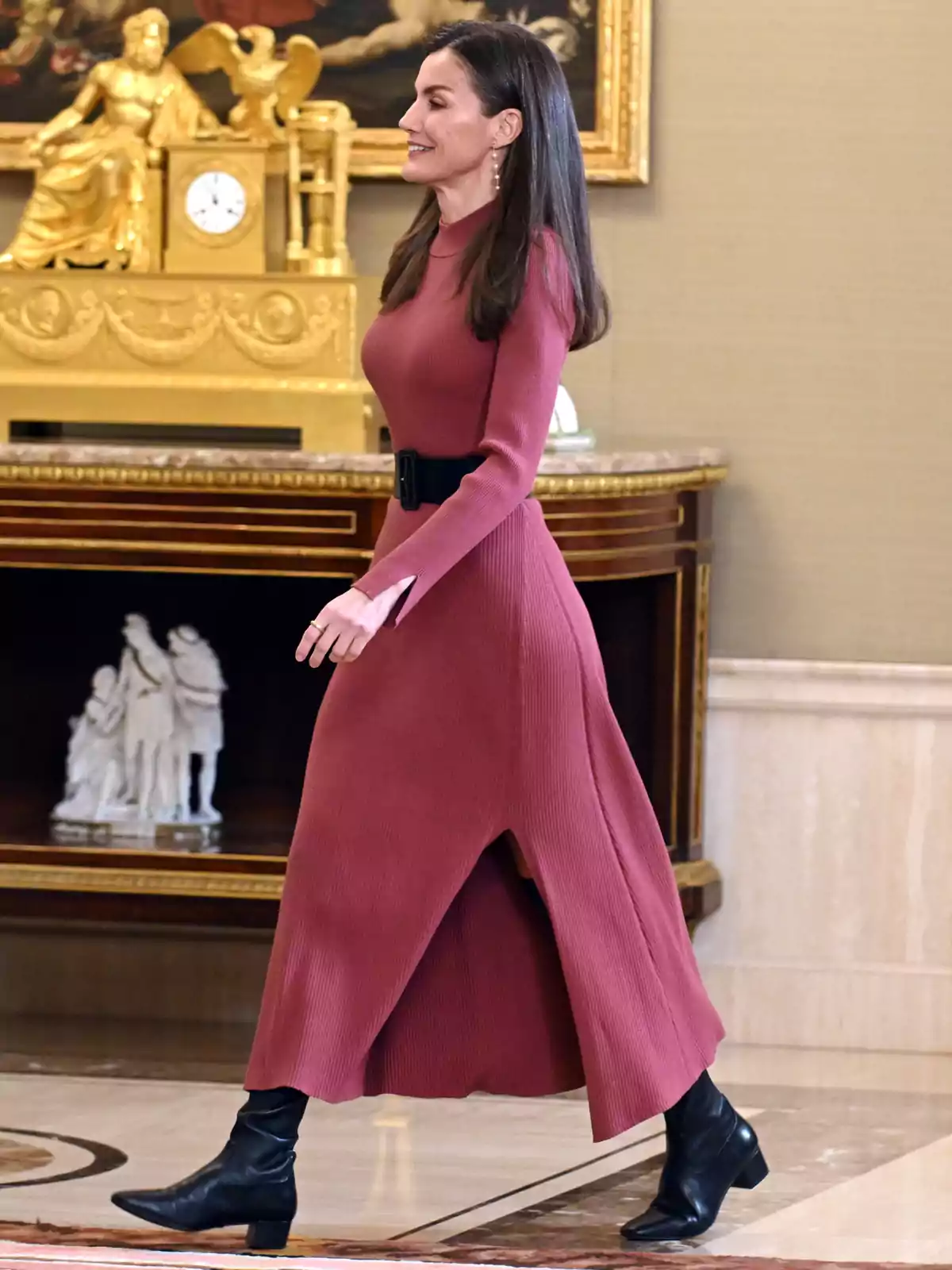 La reina Letícia caminant en una habitació elegant, vestint un vestit llarg de color rosa fosc i botes negres, amb una decoració clàssica de fons. La reina Letícia caminant en una habitació elegant, vestint un vestit llarg de color rosa fosc i botes negres, amb una decoració clàssica de fons.