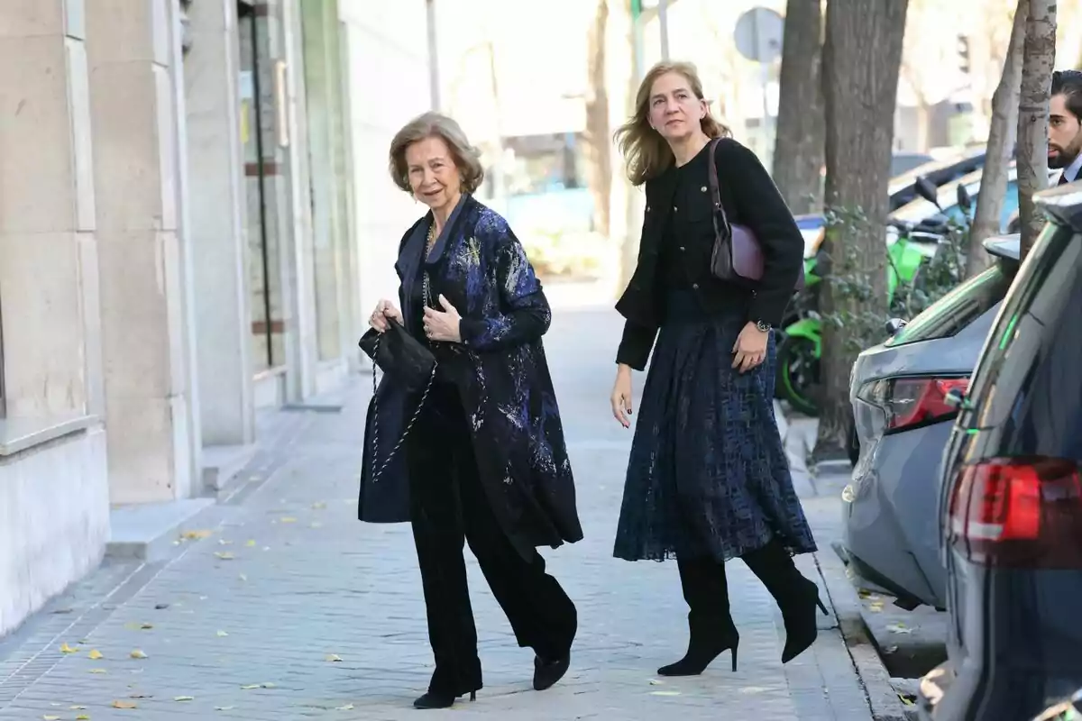 Reina Sofia i la infanta Cristina caminant per una vorera al costat d'una fila de cotxes estacionats. Reina Sofia i la infanta Cristina caminant per una vorera al costat d'una fila de cotxes estacionats.