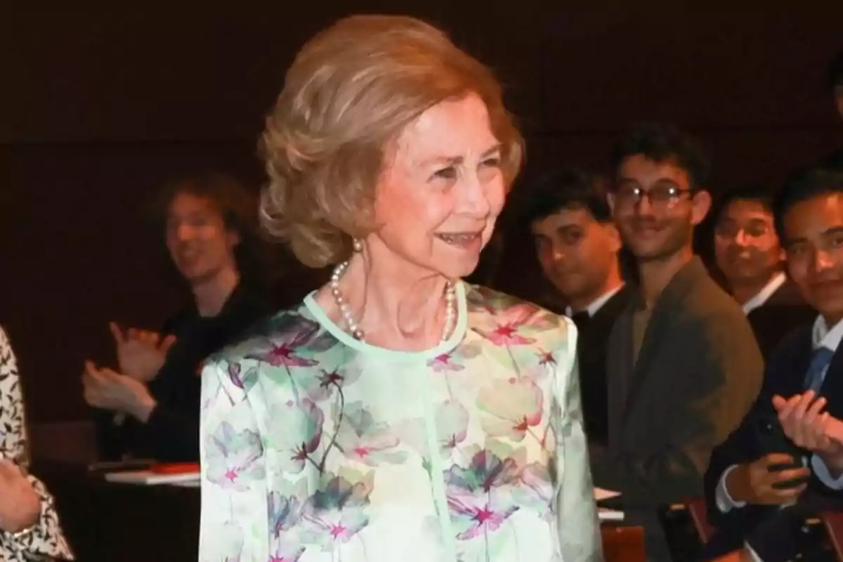 La reina Sofia amb vestit floral somriu mentre diverses persones l'observen i aplaudeixen en un esdeveniment. La reina Sofia amb vestit floral somriu mentre diverses persones l'observen i aplaudeixen en un esdeveniment.