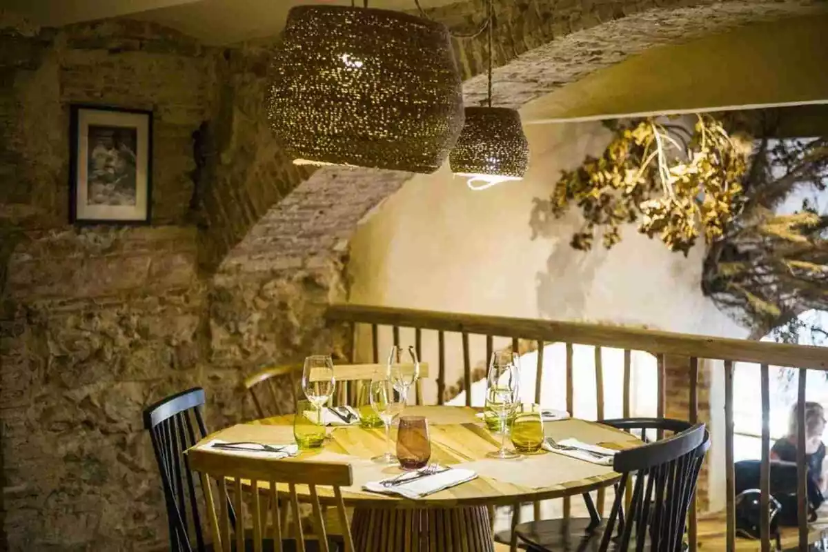 Imatge del restaurant La Brutal a Girona de Marc Ribas. Imatge d'un restaurant rústic amb un a taula rodona y cuatre cadires. La taula està parala amb coberts, gots i copes