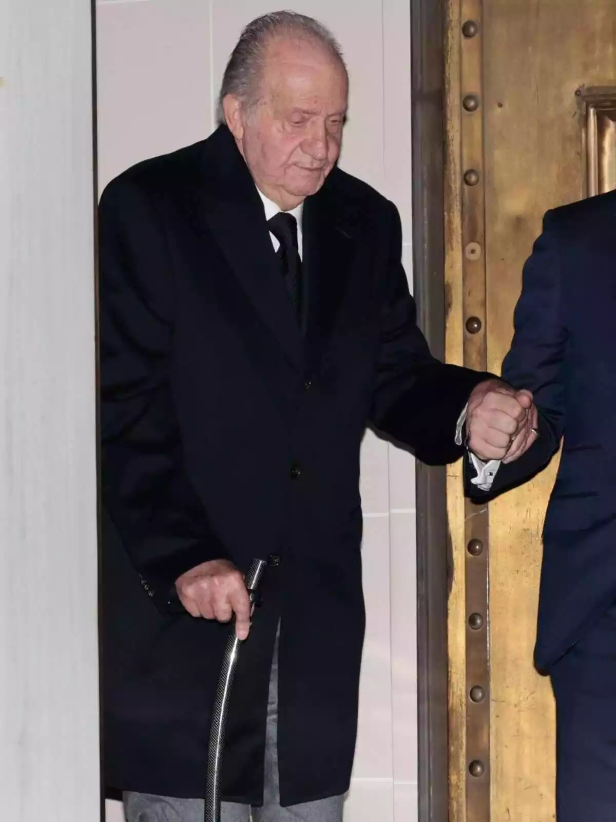El Rei Juan Carlos I caminant amb l'ajuda d'un bastó i d'un home