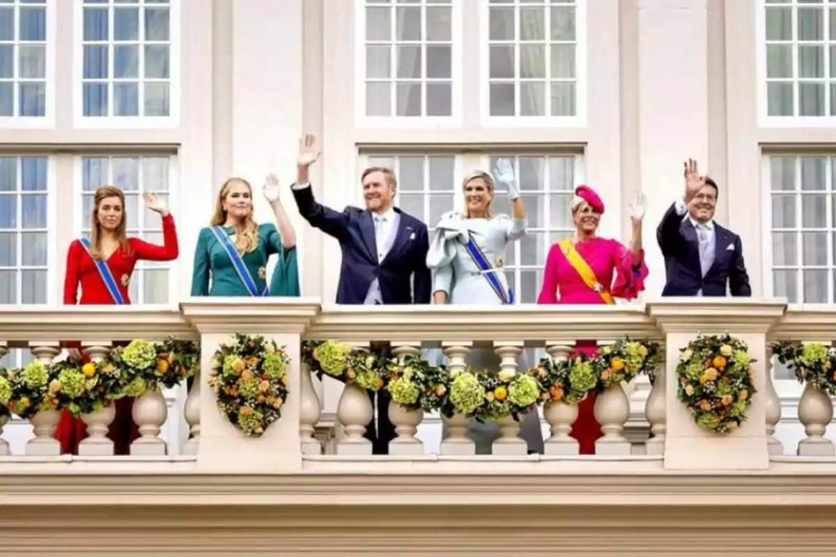 Un grup de persones vestides elegantment saluda des d'un balcó adornat amb garlandes de flors, davant d'una façana amb grans finestres. Un grup de persones vestides elegantment saluda des d'un balcó adornat amb garlandes de flors, davant d'una façana amb grans finestres.