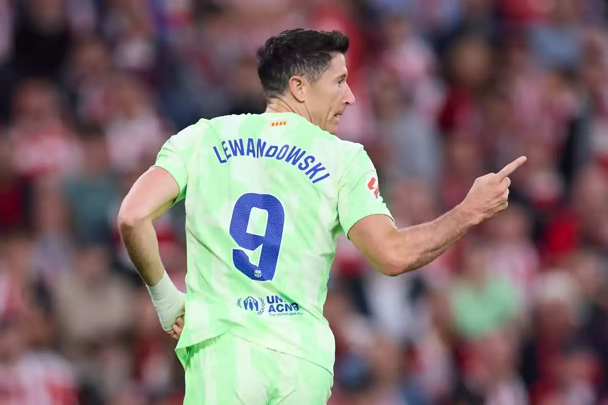 Futbolista con uniforme verde claro y el número 9 en la espalda señalando hacia la derecha en un estadio lleno de espectadores