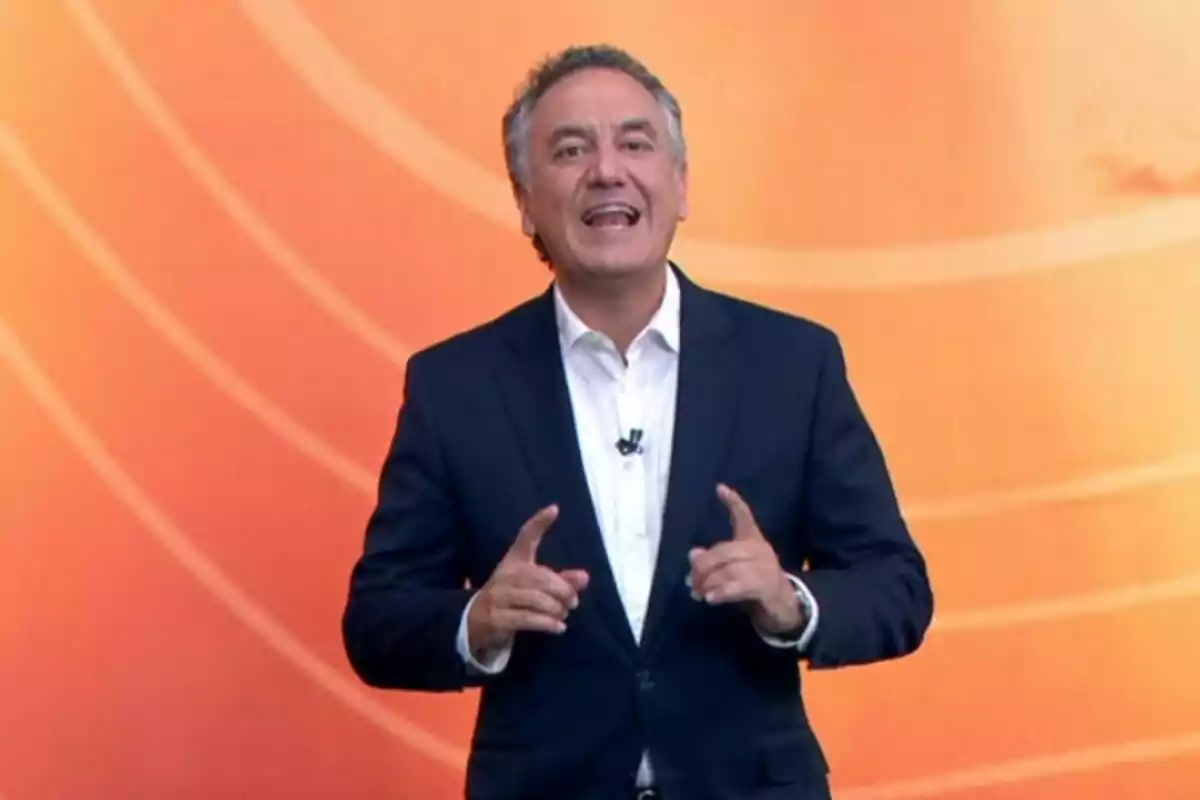 Pla mitjà de Roberto Brasero vestit amb vestit fosc i camisa blanca parlant davant d’un fons taronja. Pla mitjà de Roberto Brasero vestit amb vestit fosc i camisa blanca parlant davant d’un fons taronja.