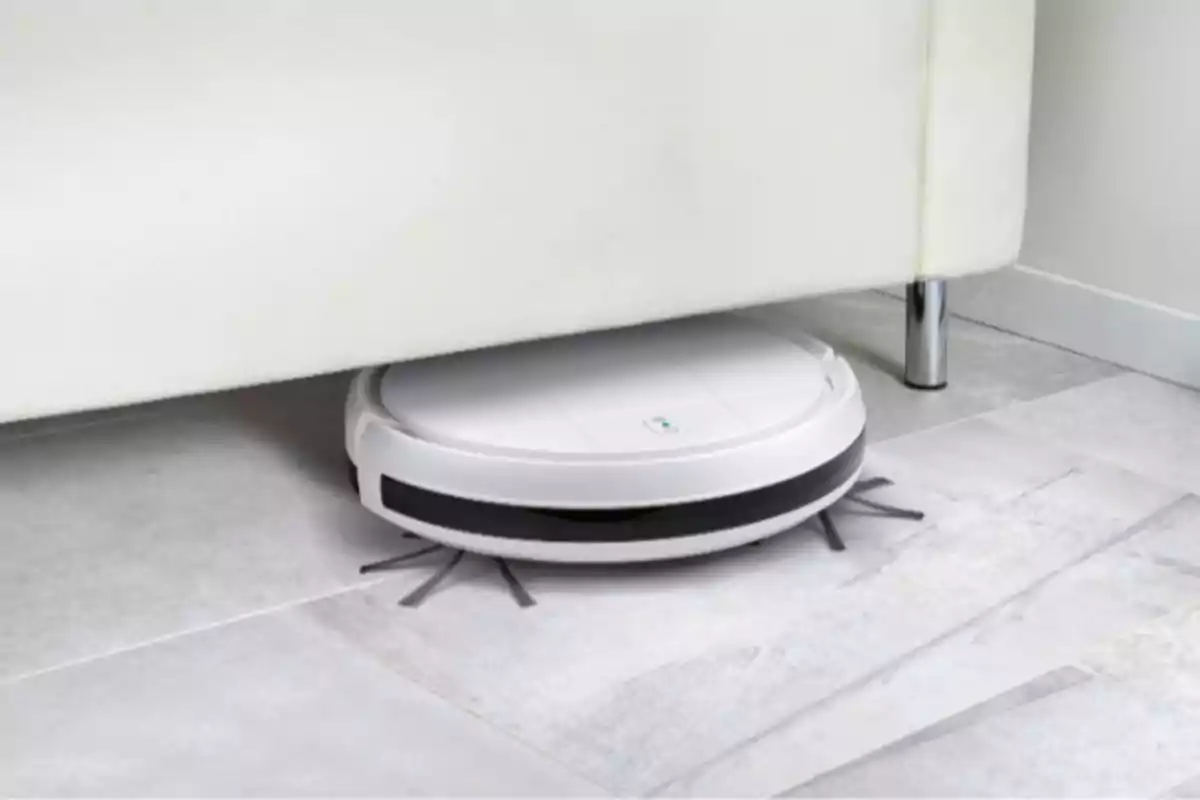 Un robot aspirador blanc netejant sota un sofà en un terra de rajoles clares. Un robot aspirador blanc netejant sota un sofà en un terra de rajoles clares.