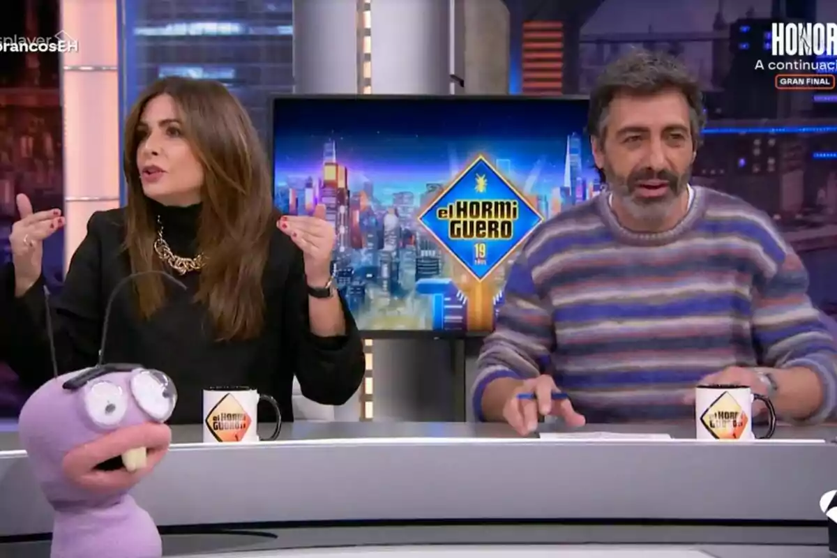 Nuria Roca i Juan del Val asseguts en un plató de televisió amb una titella i tasses amb el logotip de Nuria Roca i Juan del Val asseguts en un plató de televisió amb una titella i tasses amb el logotip de