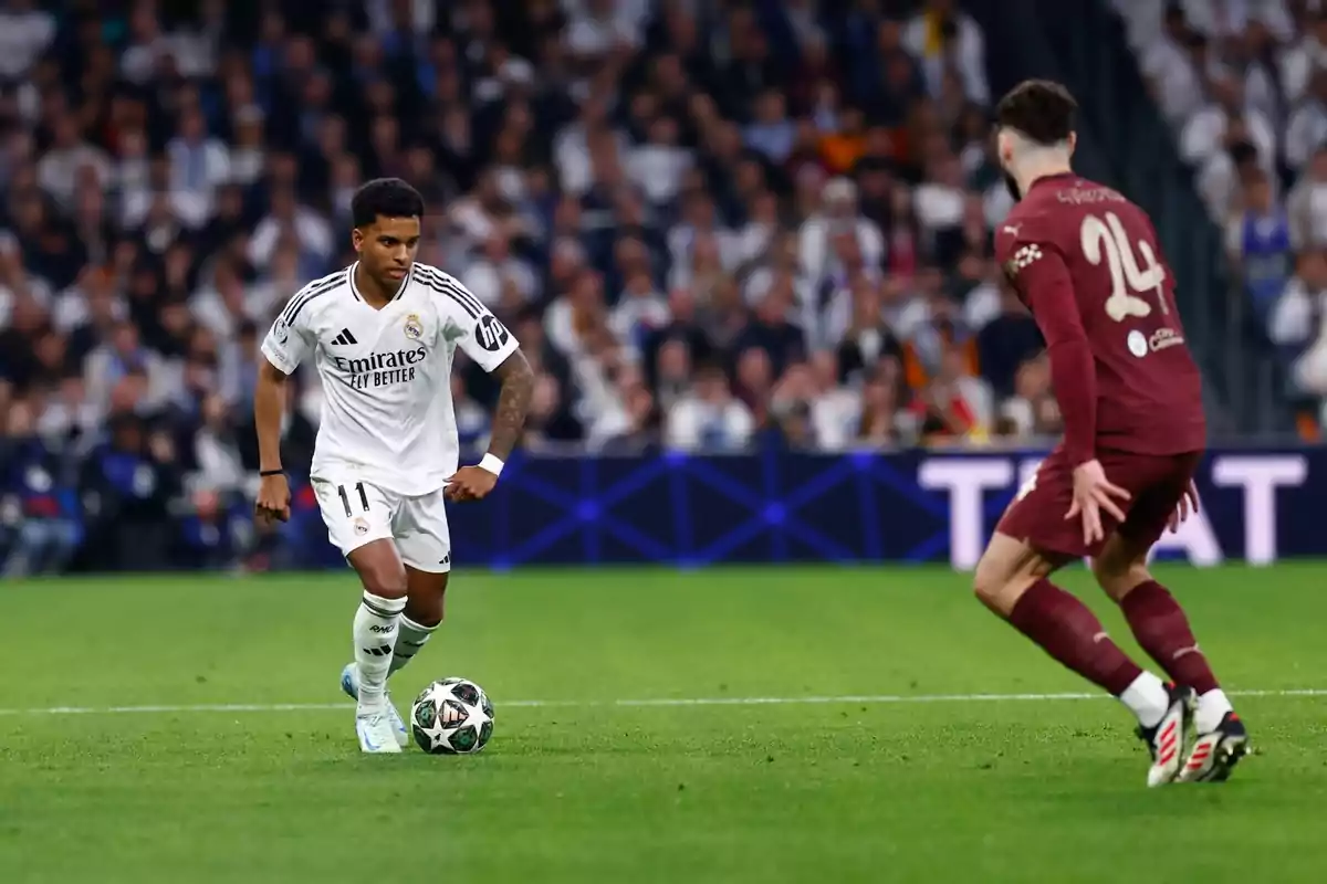 Un jugador de fútbol con uniforme blanco controla el balón mientras un oponente con uniforme marrón se acerca en un estadio lleno de espectadores. Un jugador de fútbol con uniforme blanco controla el balón mientras un oponente con uniforme marrón se acerca en un estadio lleno de espectadores.