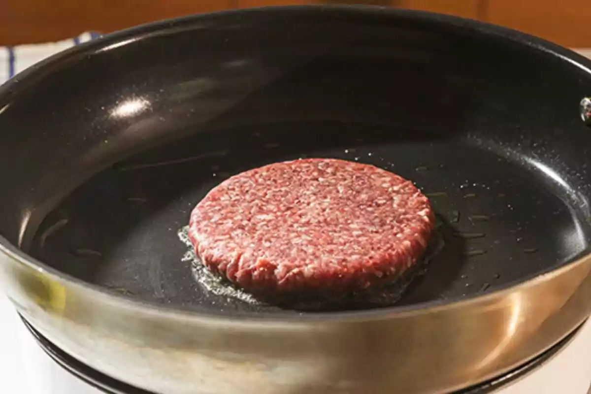 Hamburguesa crua cuinant-se en una paella amb una mica d’oli Hamburguesa crua cuinant-se en una paella amb una mica d’oli