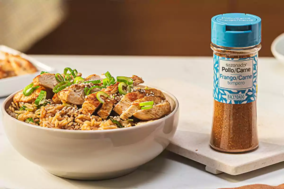 Un plat d'arròs amb pollastre i cebollí al costat d'un pot de condiment per a pollastre i carn. Un plat d'arròs amb pollastre i cebollí al costat d'un pot de condiment per a pollastre i carn.