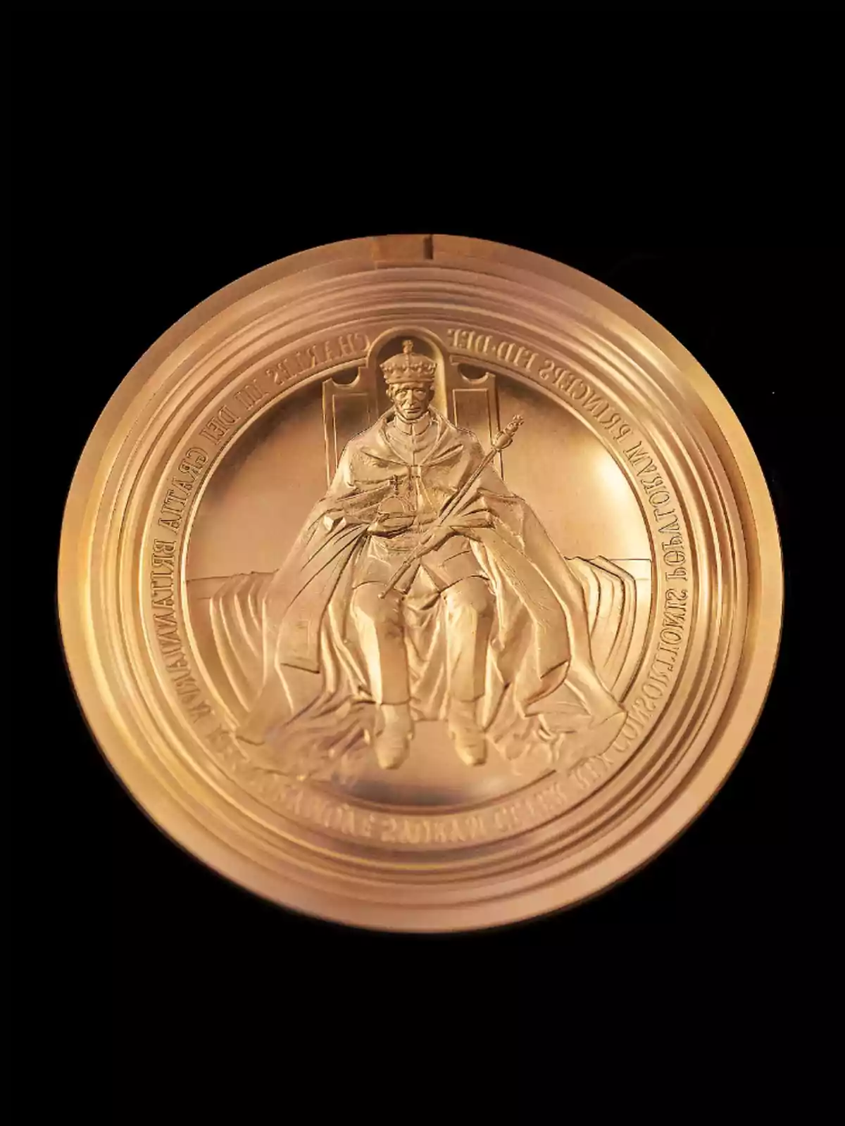 Una medalla daurada amb un disseny en relleu d'una figura asseguda en un tron sostenint un ceptre, envoltada d'inscripcions a la vora. Una medalla daurada amb un disseny en relleu d'una figura asseguda en un tron sostenint un ceptre, envoltada d'inscripcions a la vora.