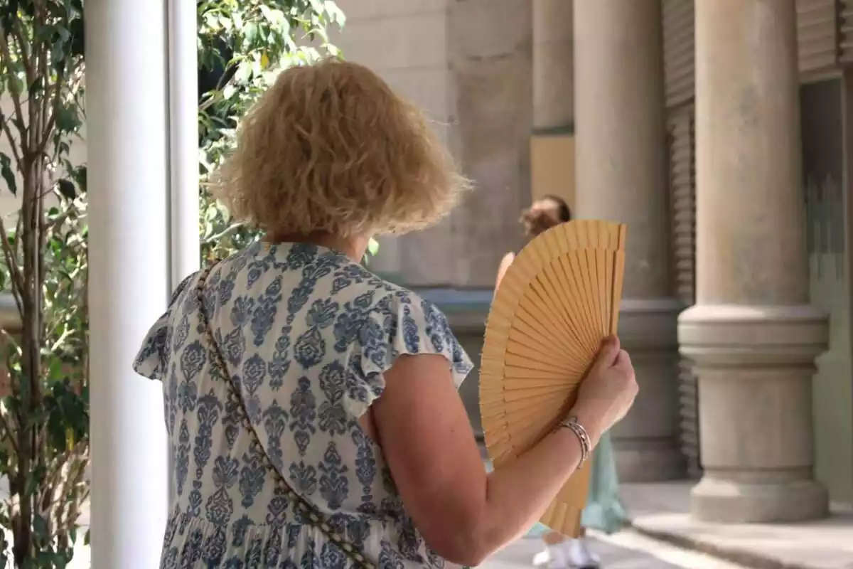 Una senyora d'esquena ventant-se amb un ventall per la calor Una senyora d'esquena ventant-se amb un ventall per la calor