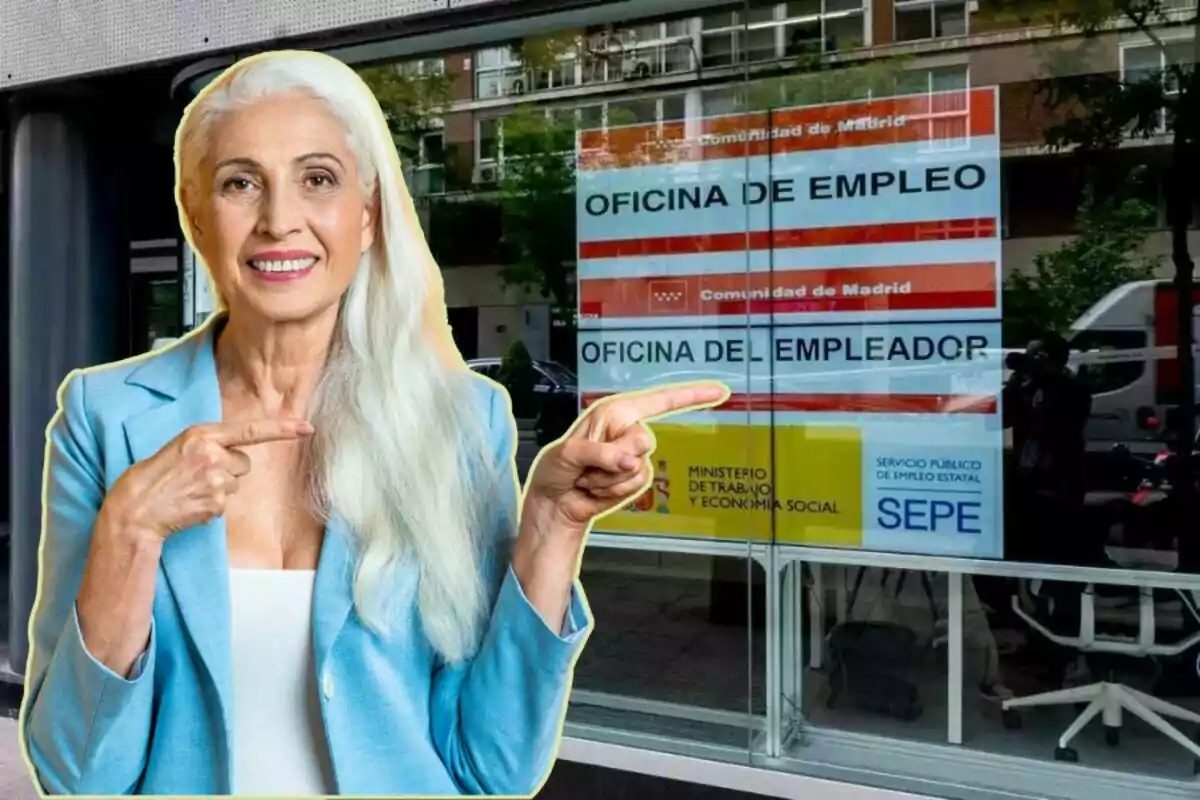 Una dona de cabell canós i vestida amb un blazer blau és somrient i assenyalant amb tots dos dits índexs cap a un cartell de l'Oficina d'Ocupació de la Comunitat de Madrid, visible a través d'una finestra.