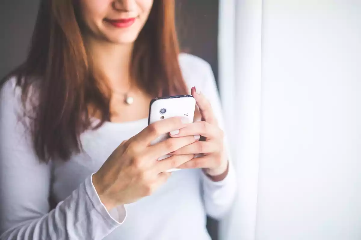 Woman with brown hair using a white mobile phone and smiling. Woman with brown hair using a white mobile phone and smiling.