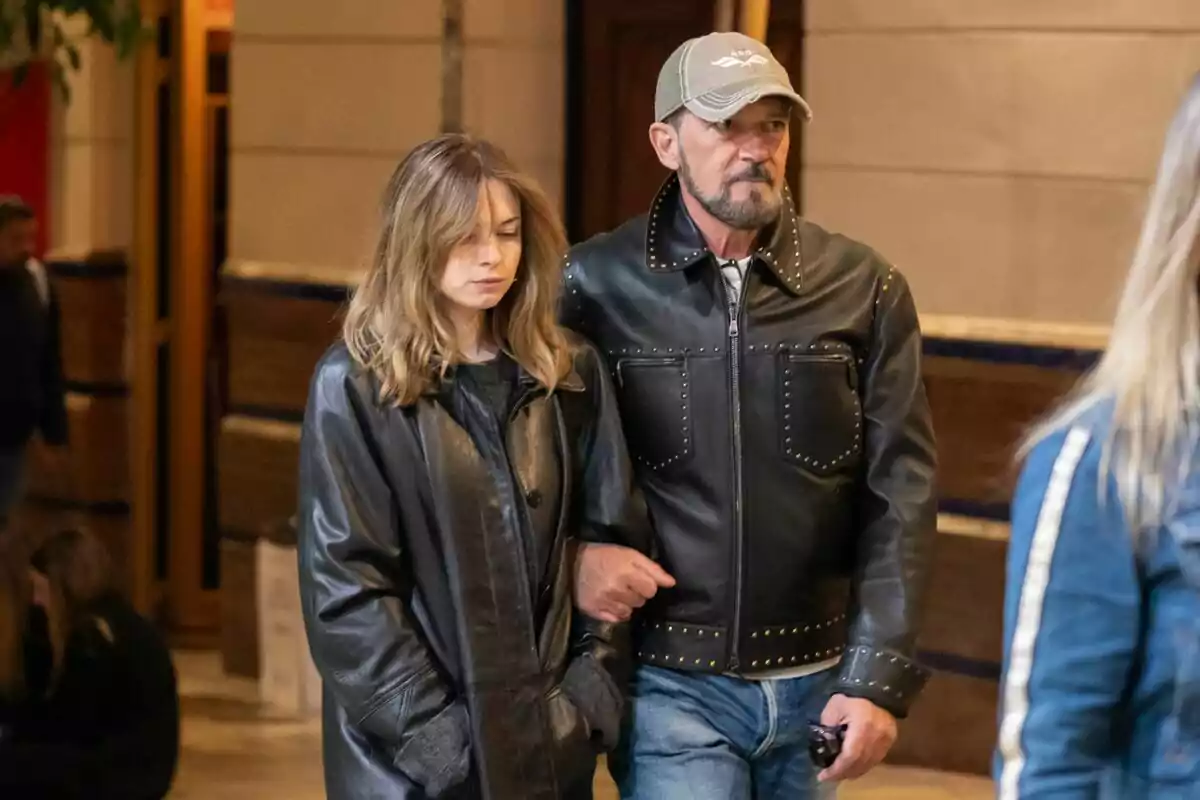 Stella del Carmen Banderas y Antonio Banderas caminando juntos, ambos con chaquetas de cuero, el hombre lleva una gorra y la mujer tiene el cabello suelto.