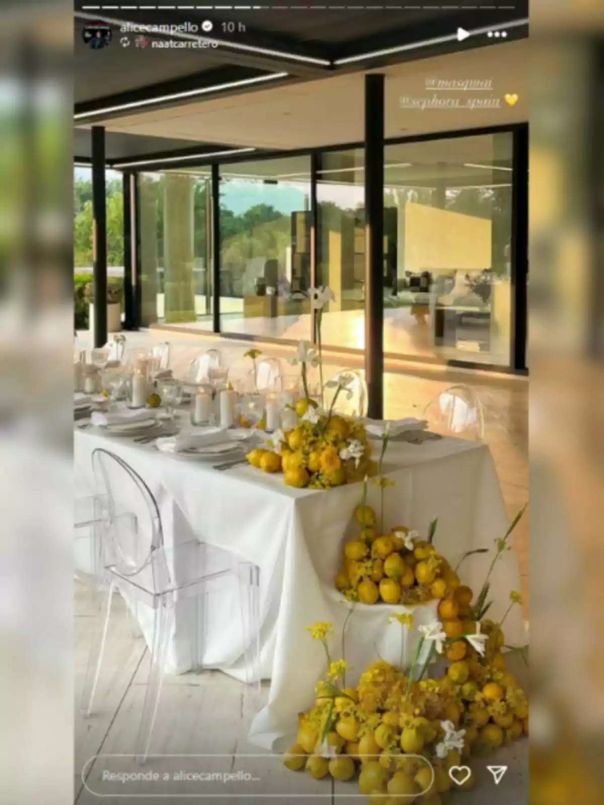 Taula elegant decorada amb llimones i flors grogues en un espai modern amb parets de vidre i cadires transparents Taula elegant decorada amb llimones i flors grogues en un espai modern amb parets de vidre i cadires transparents