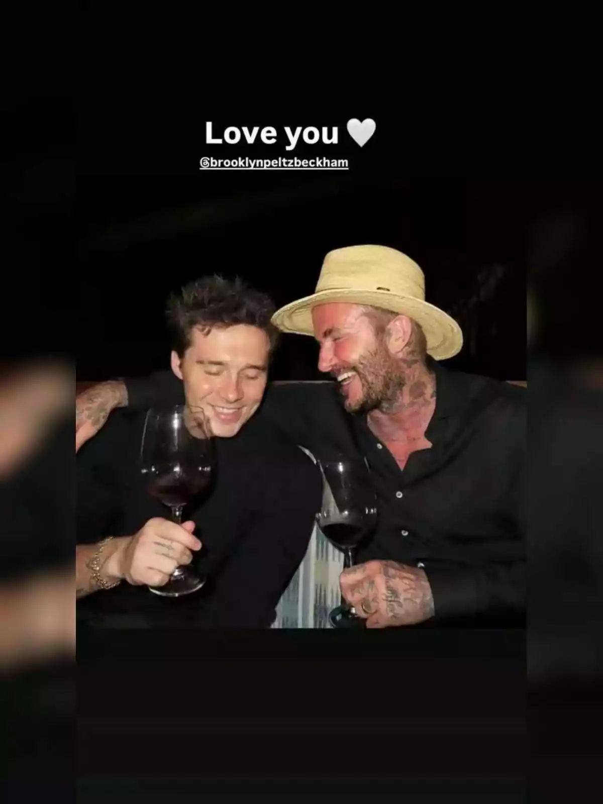 Brooklyn and David Beckham smile and hug while holding glasses of red wine; one of them is wearing a hat and both are dressed in black. The atmosphere is relaxed and cheerful. Brooklyn and David Beckham smile and hug while holding glasses of red wine; one of them is wearing a hat and both are dressed in black. The atmosphere is relaxed and cheerful.
