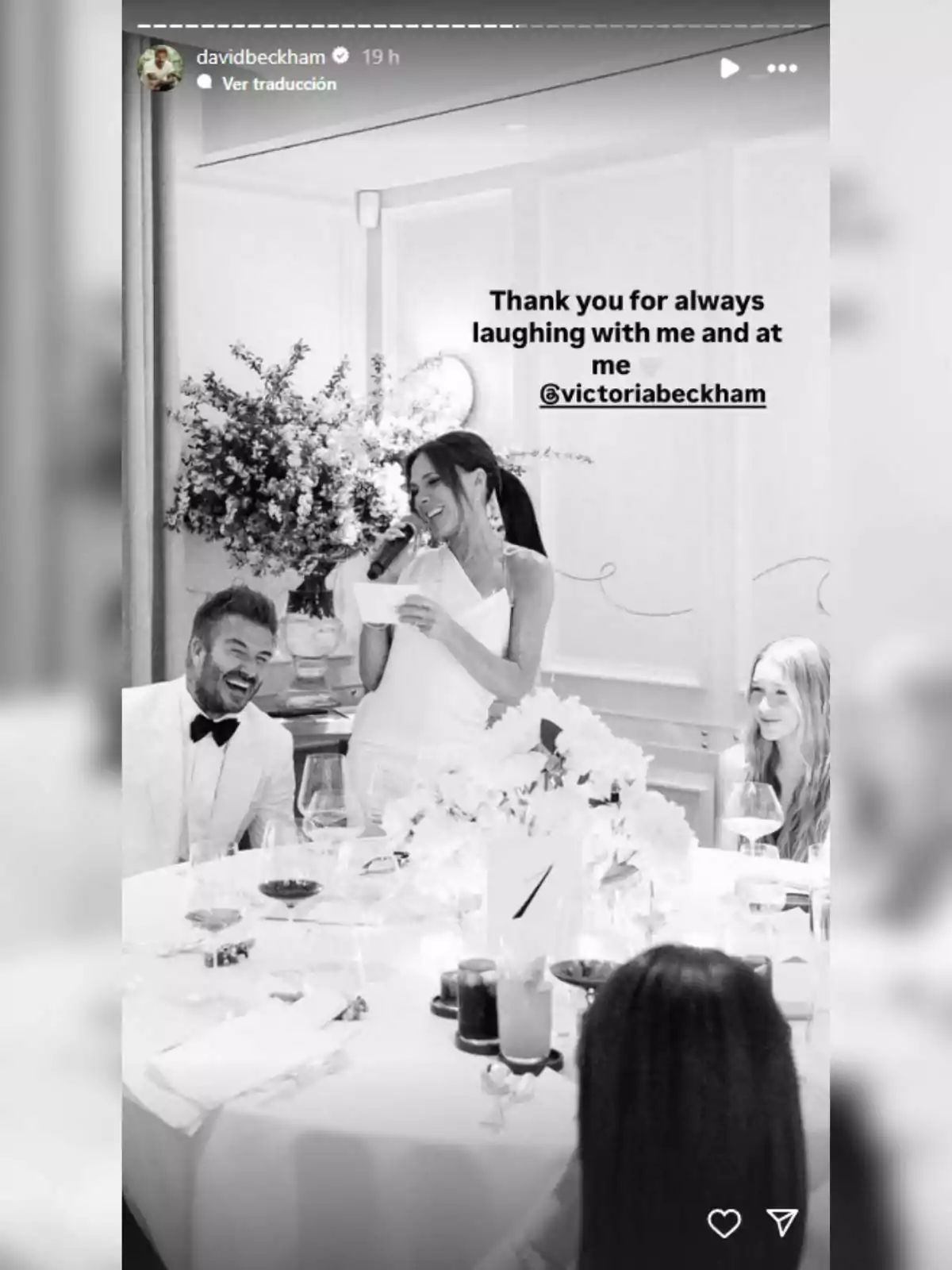 Victoria Beckham somriu mentre sosté un micròfon en un sopar elegant, acompanyada de persones que també riuen. Victoria Beckham somriu mentre sosté un micròfon en un sopar elegant, acompanyada de persones que també riuen.